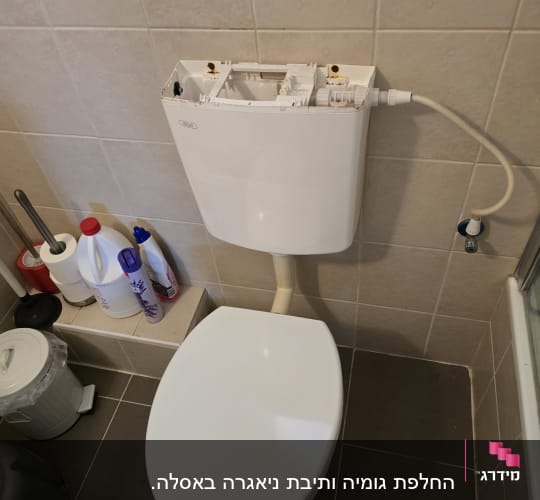 אסלה עם מיכל הדחה פתוח וכלי ניקוי בחדר אמבטיה